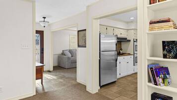 A modern kitchen with a built-in refrigerator, a gas stove, and white cabinetry. There is a bookshelf with books and a framed picture on the wall.