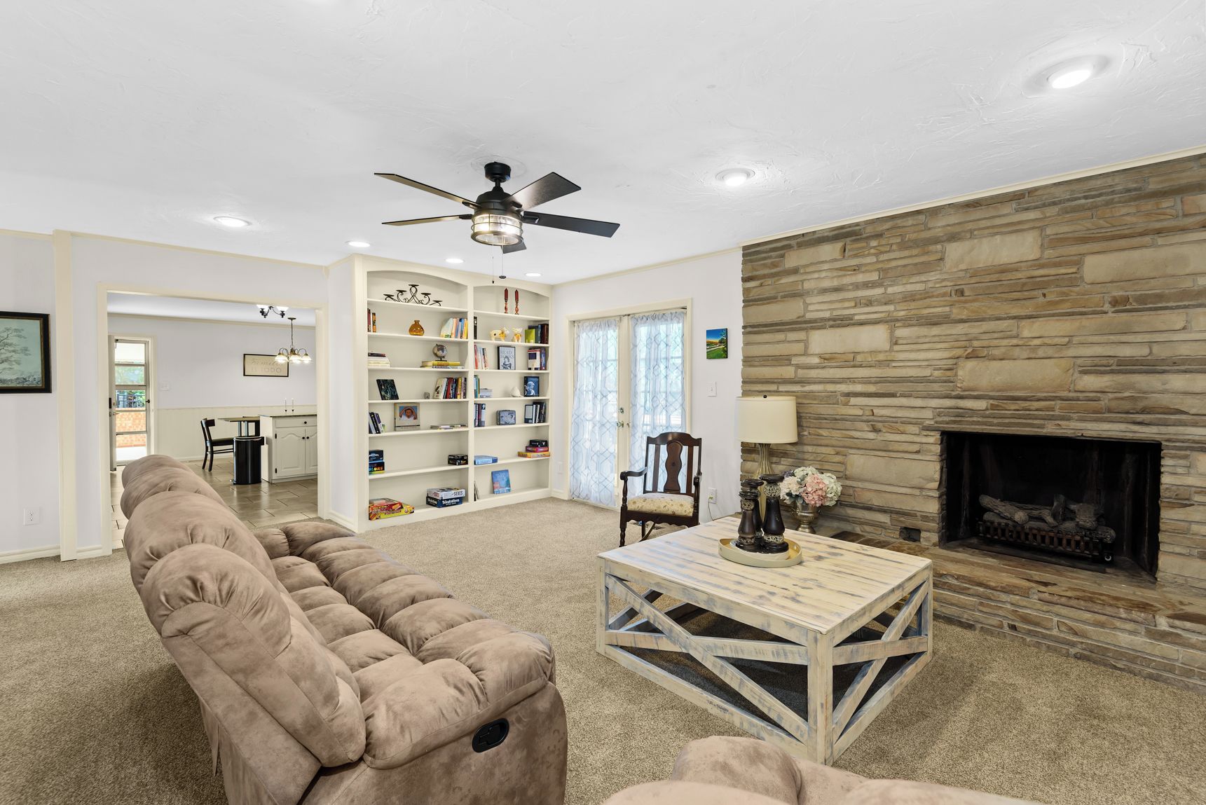 A living room with a beige sofa, a wooden coffee table, a fireplace, and a bookshelf.