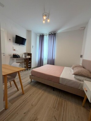 Un dormitorio moderno con una cama, un escritorio, una silla y un televisor montado en la pared.