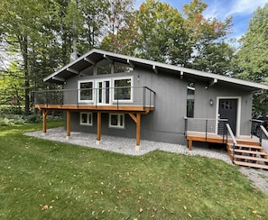 Une maison moderne à deux étages, dotée d’un balcon, d’une terrasse en bois et d’une allée gravillonnée.