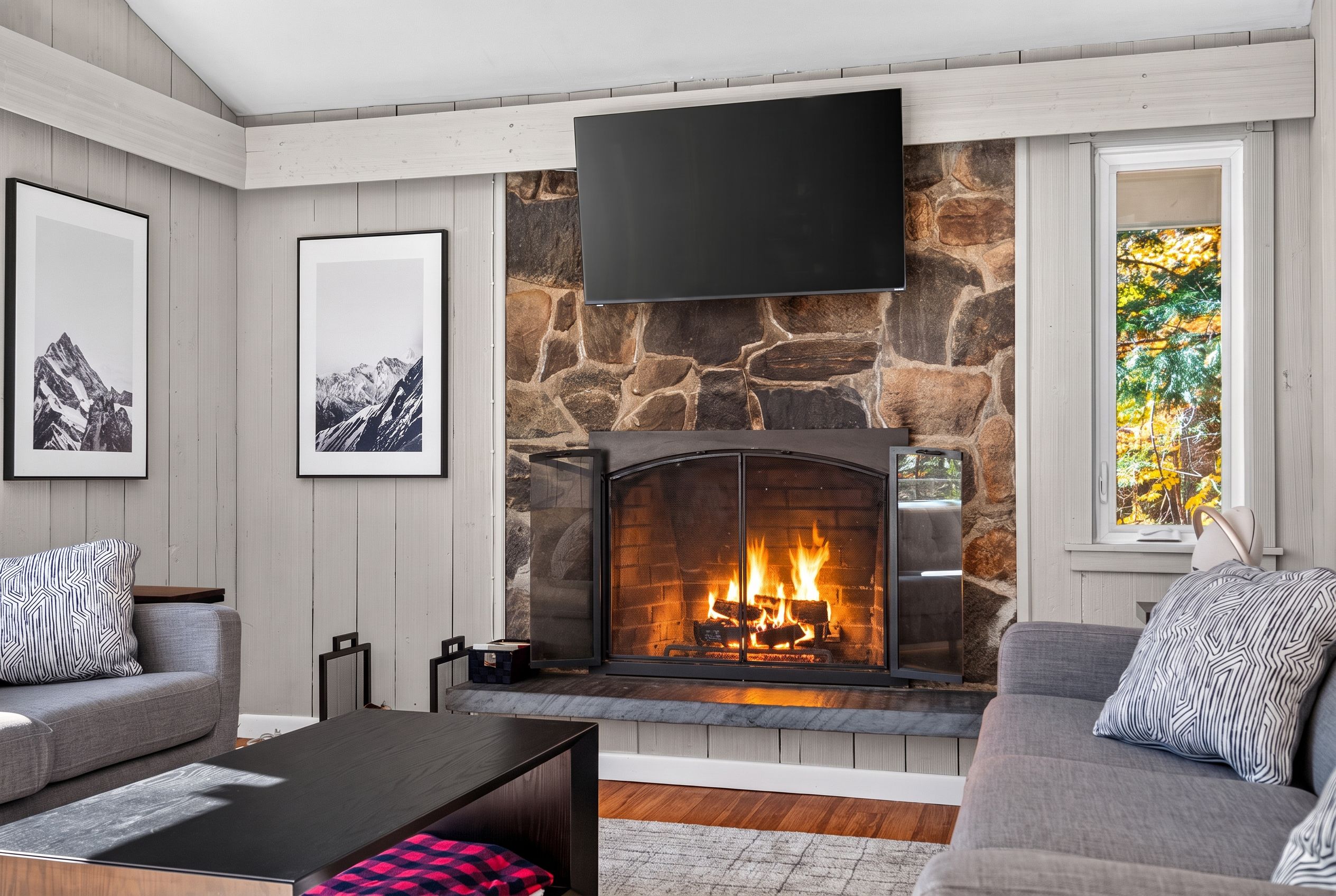 A modern living room with a stone fireplace, a flat-screen TV mounted above it, and framed pictures on the walls.