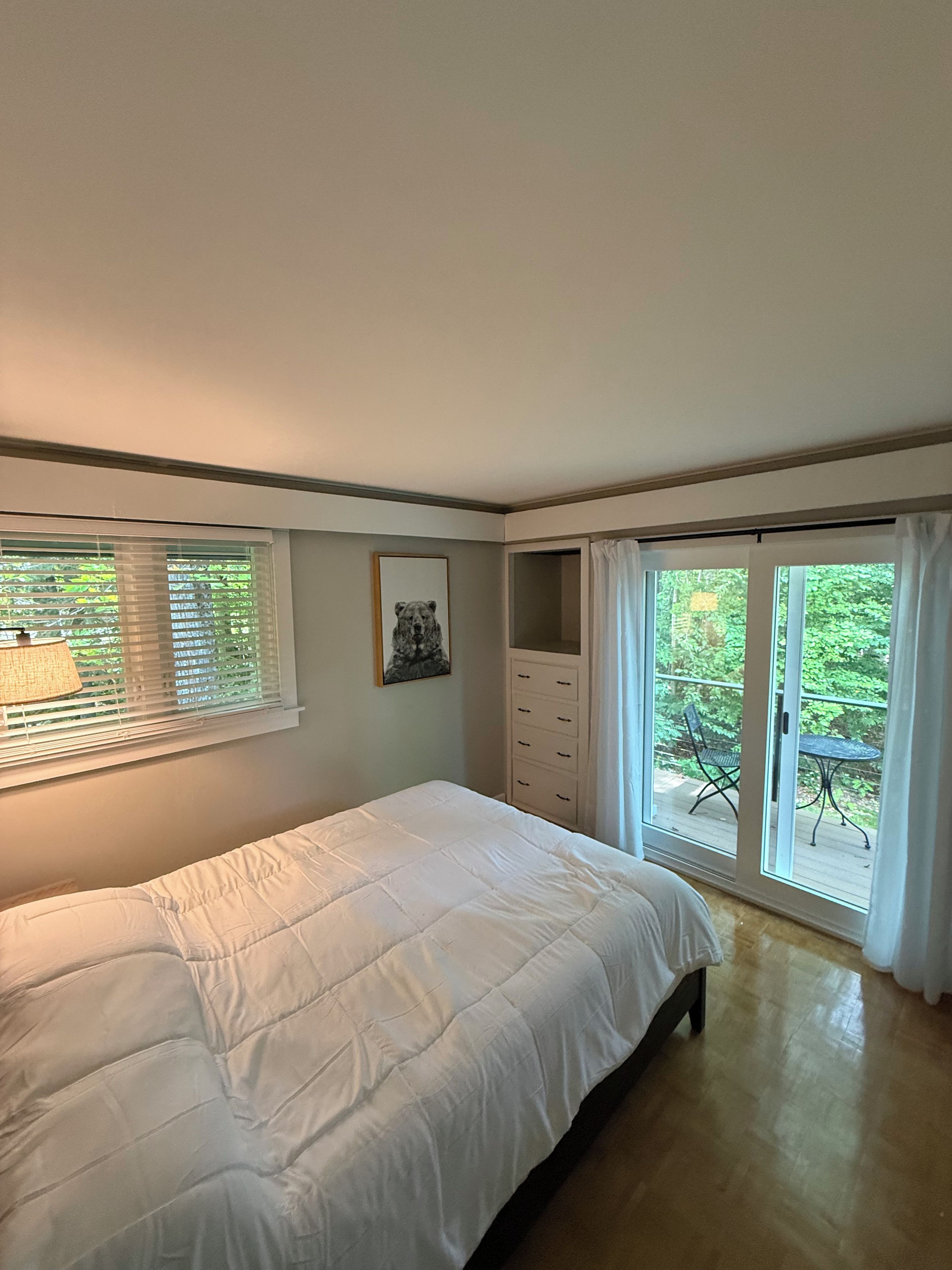 Een slaapkamer met een bed, een dressoir, een raam met zonwering en uitzicht op de omgeving.