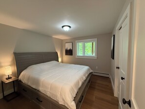 Quarto com cama, mesa de cabeceira, abajur, janela e porta.