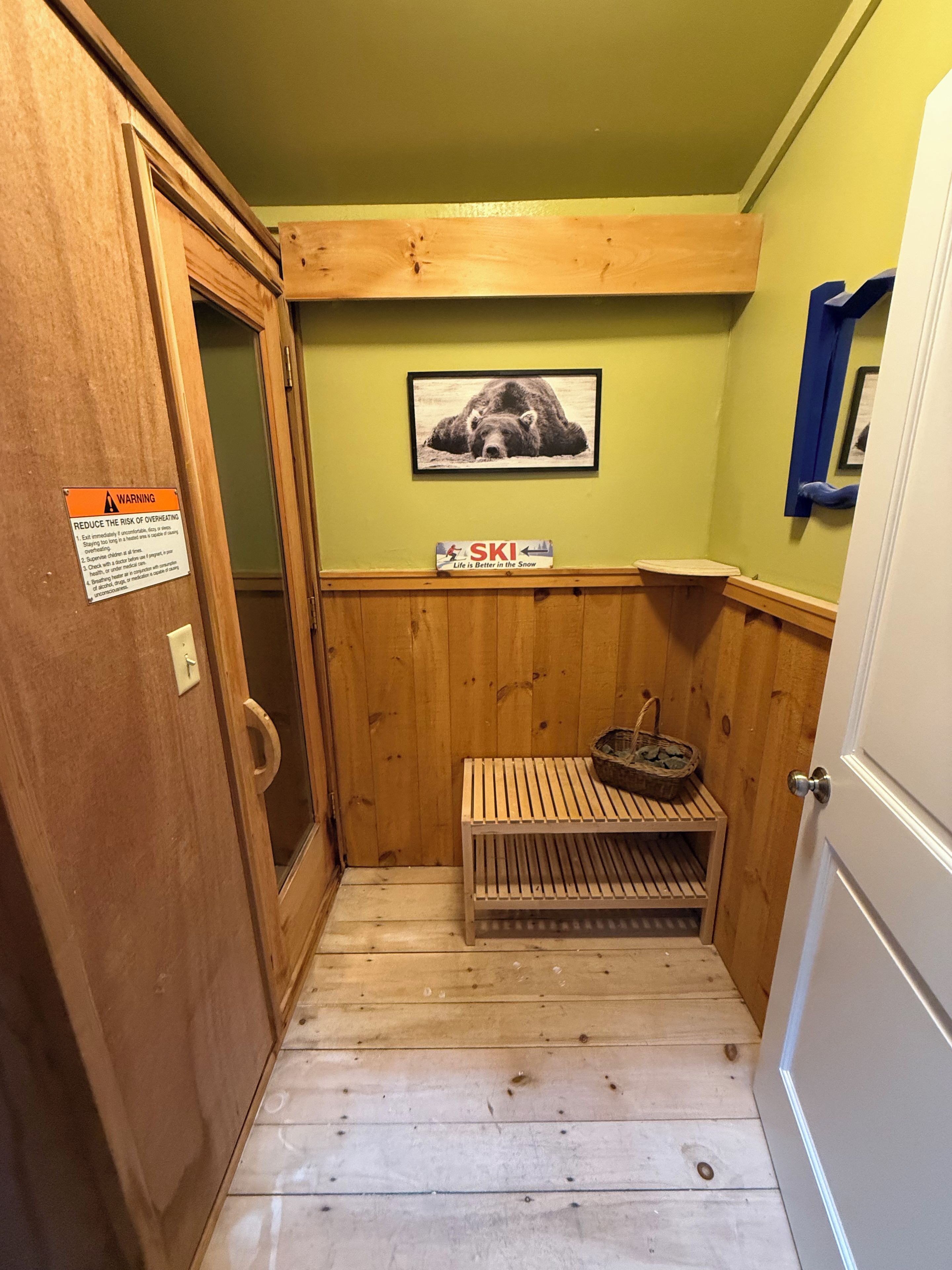 A small, narrow room with wooden walls and a wooden bench. There is a sign on the wall and a picture of a bear.