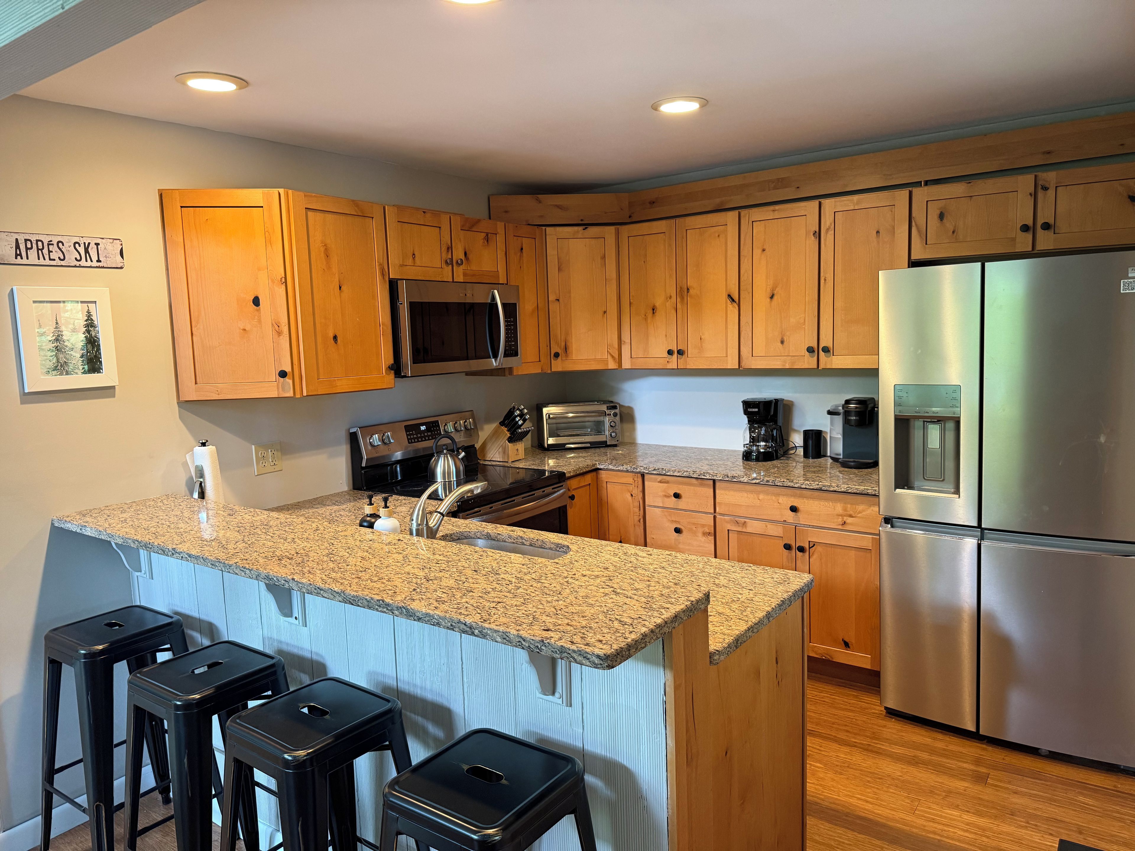 A kitchen with wooden cabinets, a stainless steel refrigerator, a microwave, a stove, and a granite countertop.