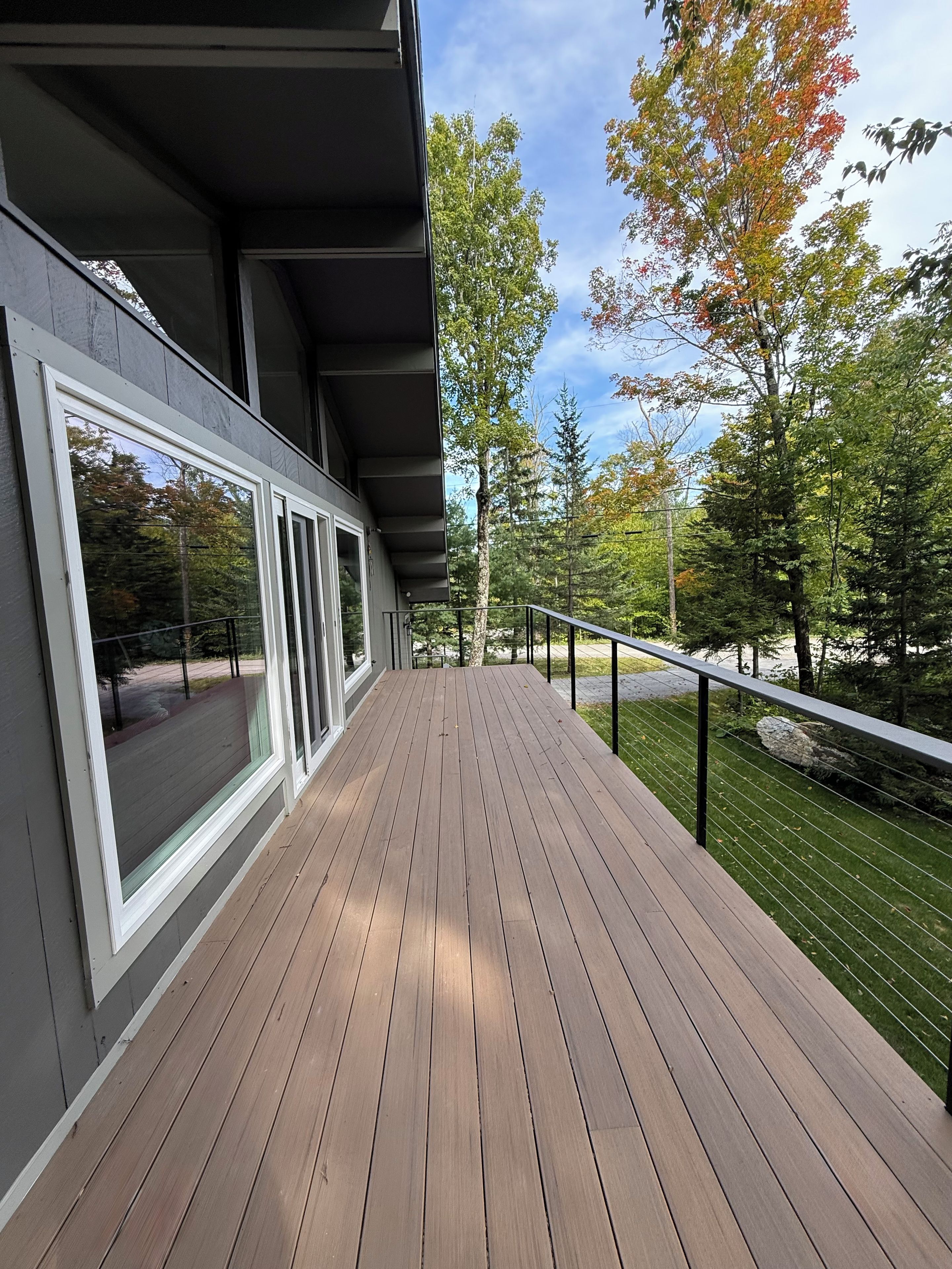 A wooden deck with a railing, overlooking a forested area.