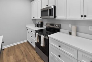 A kitchen with white cabinets, a black stove, a microwave, and a coffee maker. - Spacious Oxford Retreats with Garage & Pool (Oxford)