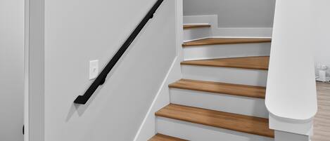 Eine Treppe mit Holzdielen und einem schwarzen Geländer, die zu einer Zwischenebene mit weißer Wand und einer Tür führt.