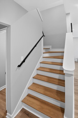 Una escalera de madera con barandilla negra, que conduce a un rellano con pared blanca y una puerta.