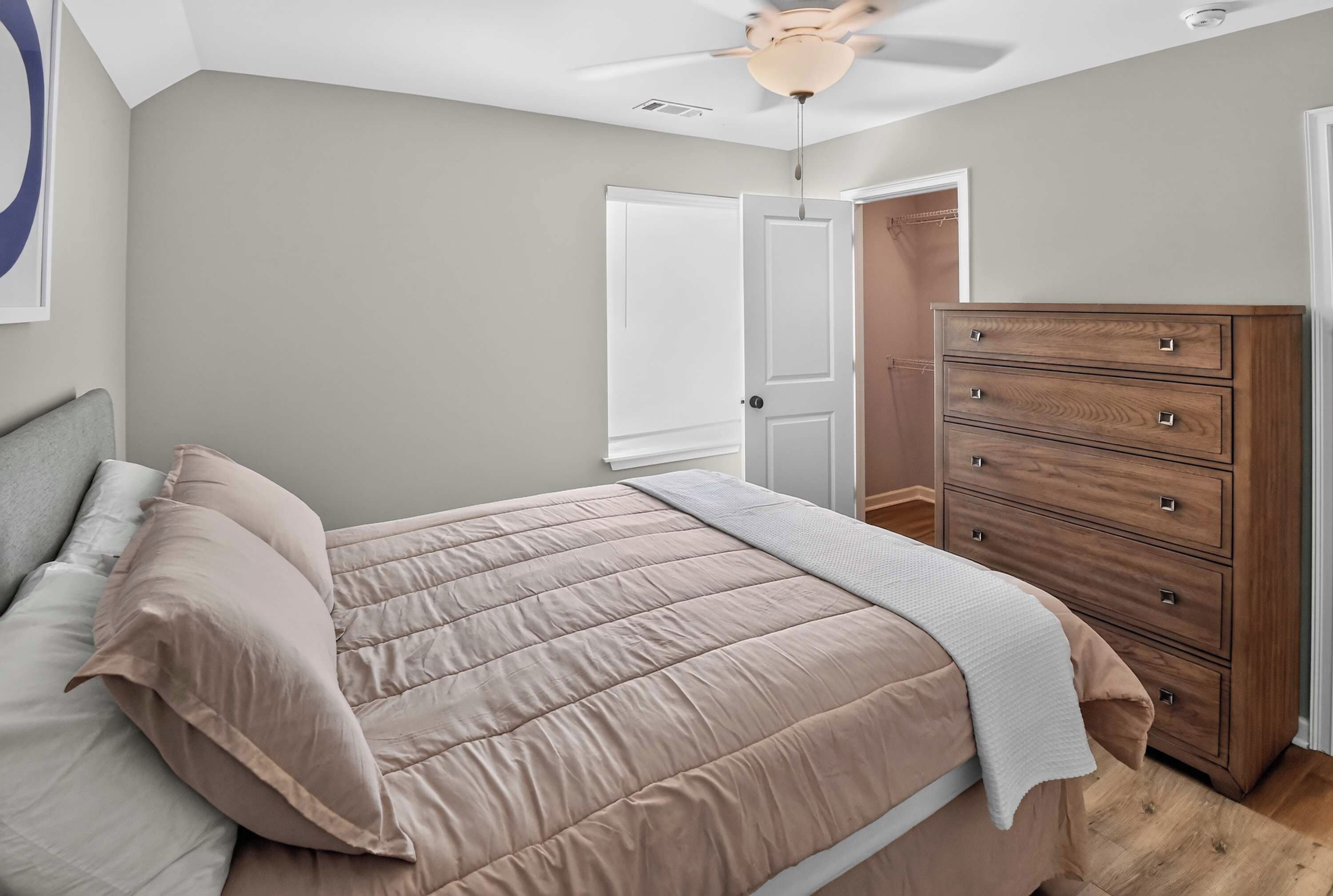 Quarto com cama, cômoda, ventilador de teto e porta que dá para outro ambiente.