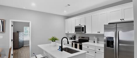 A modern kitchen with white cabinetry, stainless steel appliances, and a central island with bar stools.
