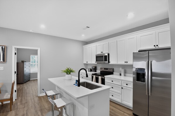 Una cocina moderna con armarios blancos, electrodomésticos de acero inoxidable y una isla central con taburetes de bar.