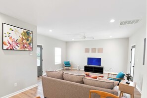A modern living room with a sectional sofa, a flat-screen TV, and a ceiling fan. - Spacious Oxford Retreats with Garage & Pool (Oxford)