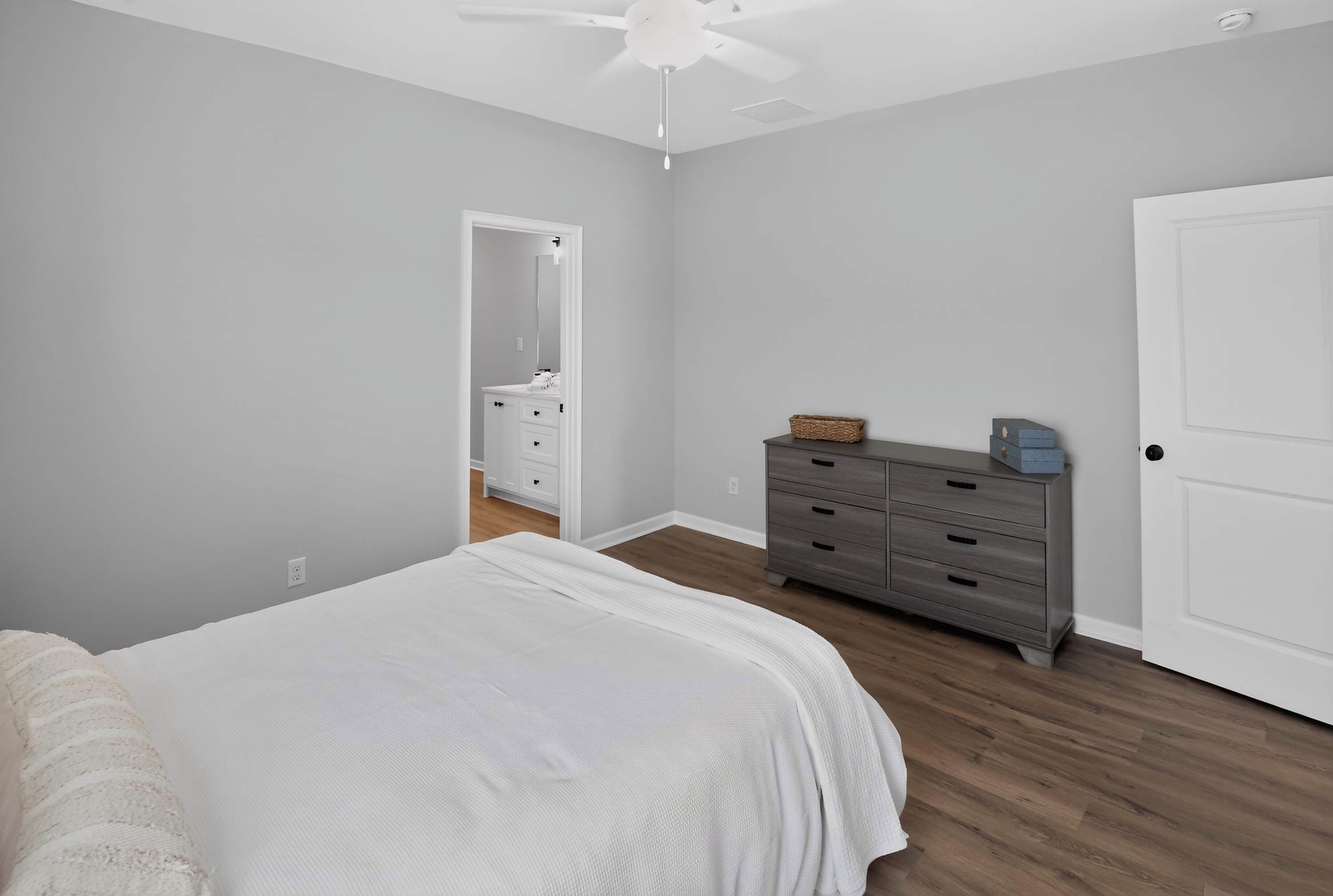 A bedroom with a bed, a dresser, a door, and a ceiling fan.