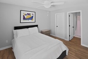 A bedroom with a bed, a ceiling fan, a nightstand, and a door leading to a bathroom.
