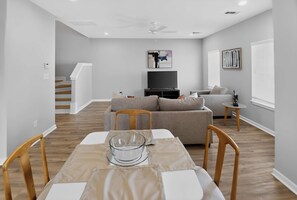 A modern living room with a dining table, sofas, and a flat-screen TV.