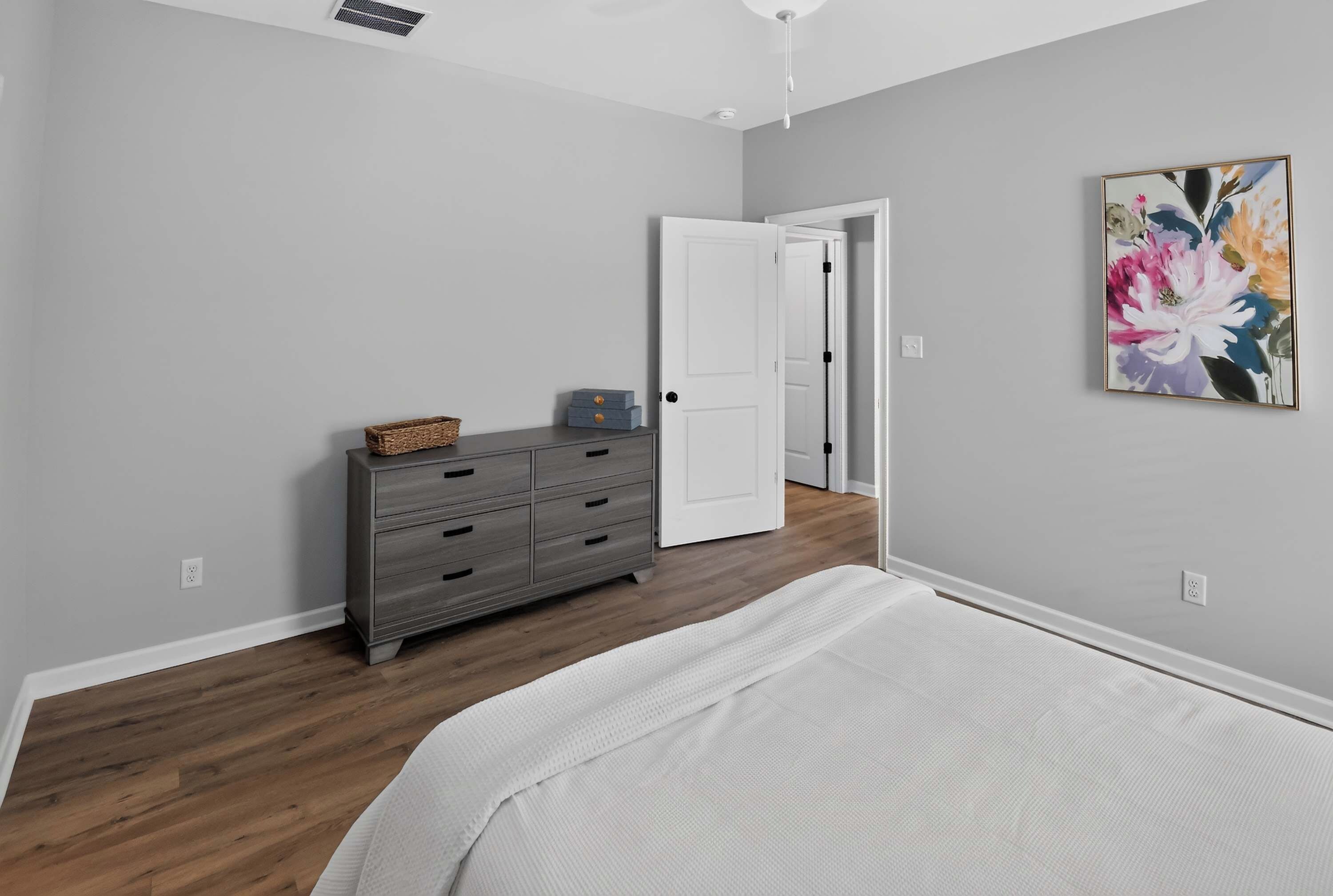 Un dormitorio con cama, cómoda, puerta y un cuadro colgado en la pared.