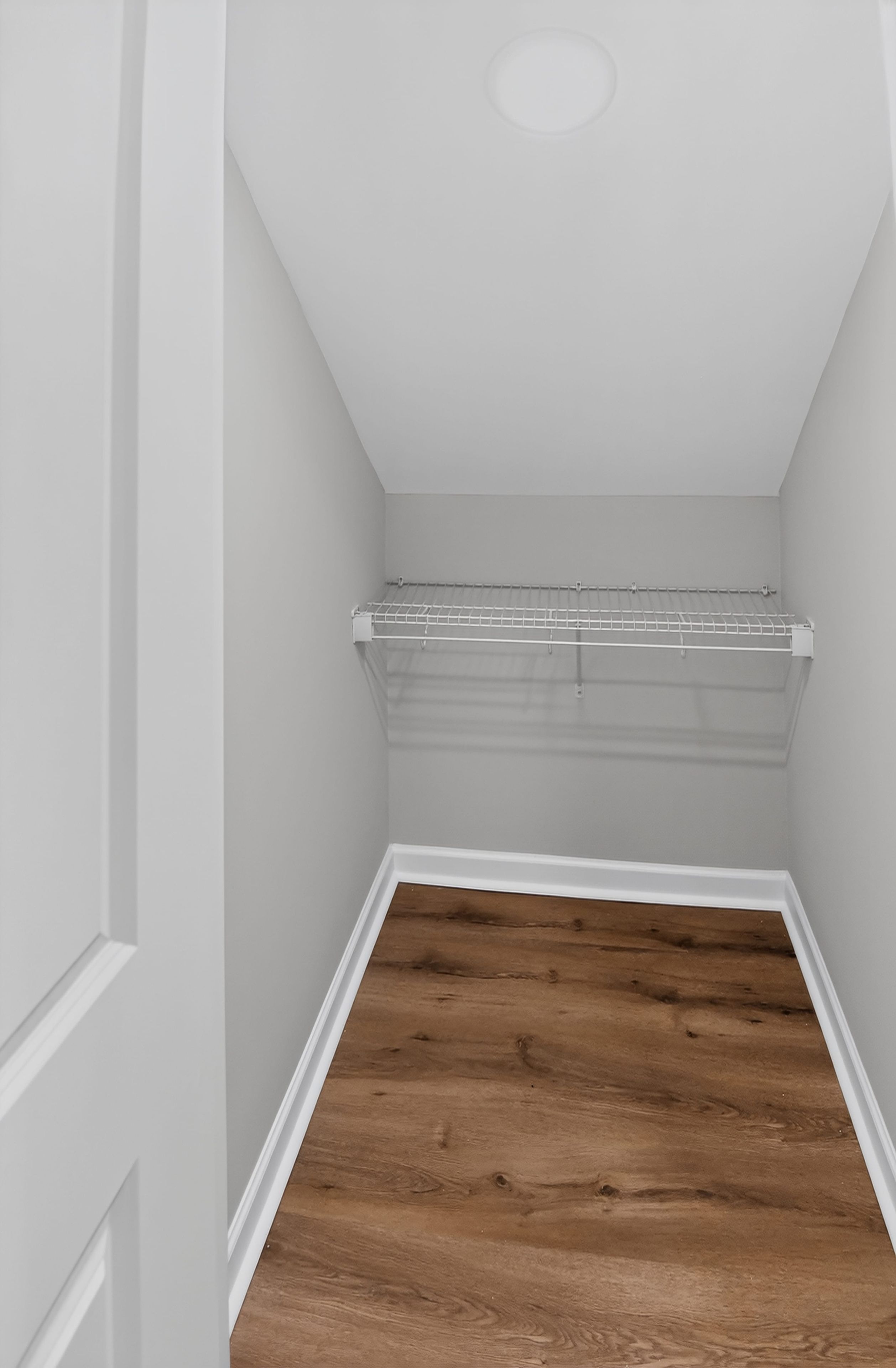 Un pasillo estrecho con suelo de madera y una puerta blanca a la izquierda.