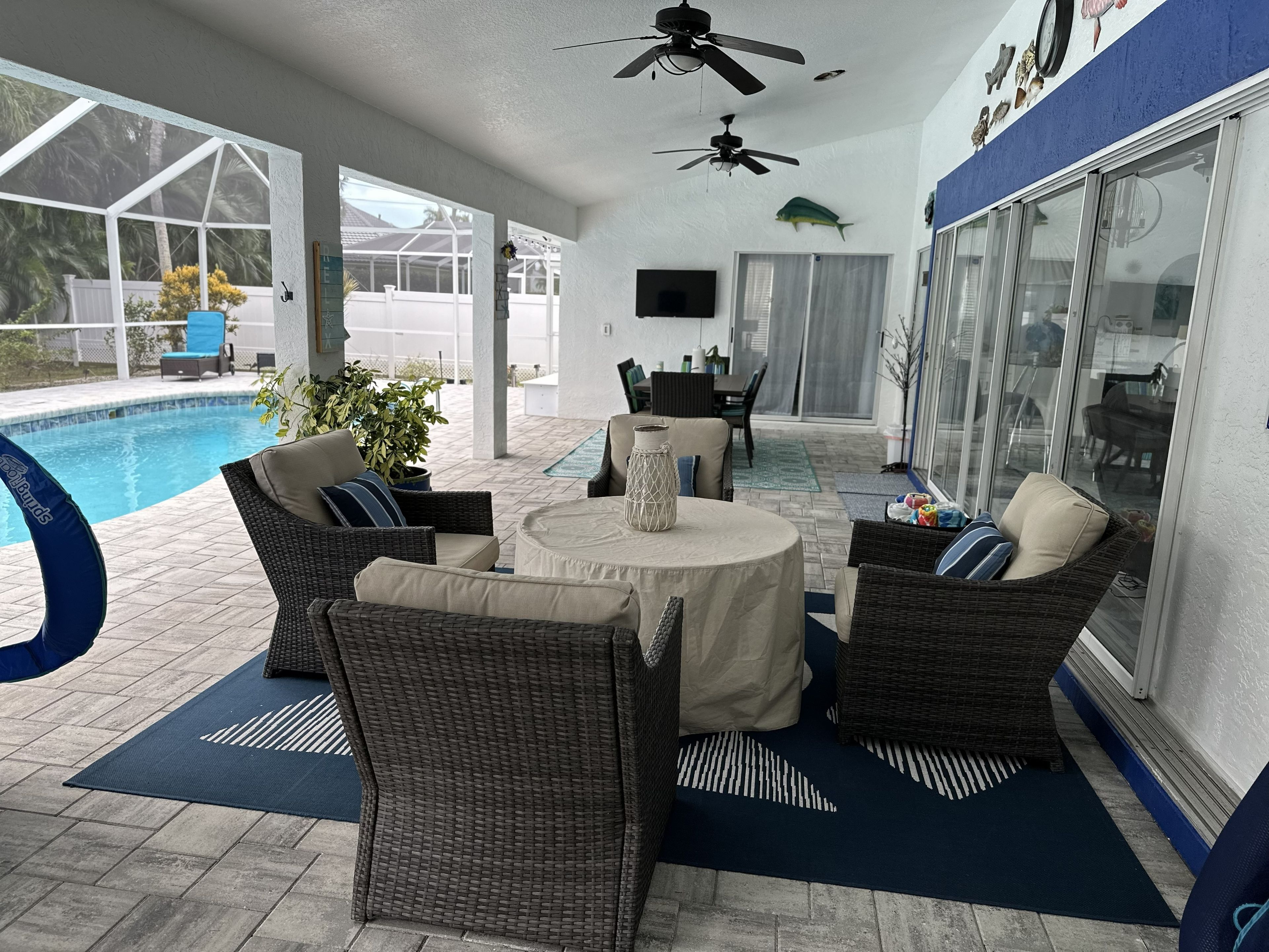Un espace extérieur abrité, aménagé avec des meubles en osier, une piscine et des ventilateurs de plafond.