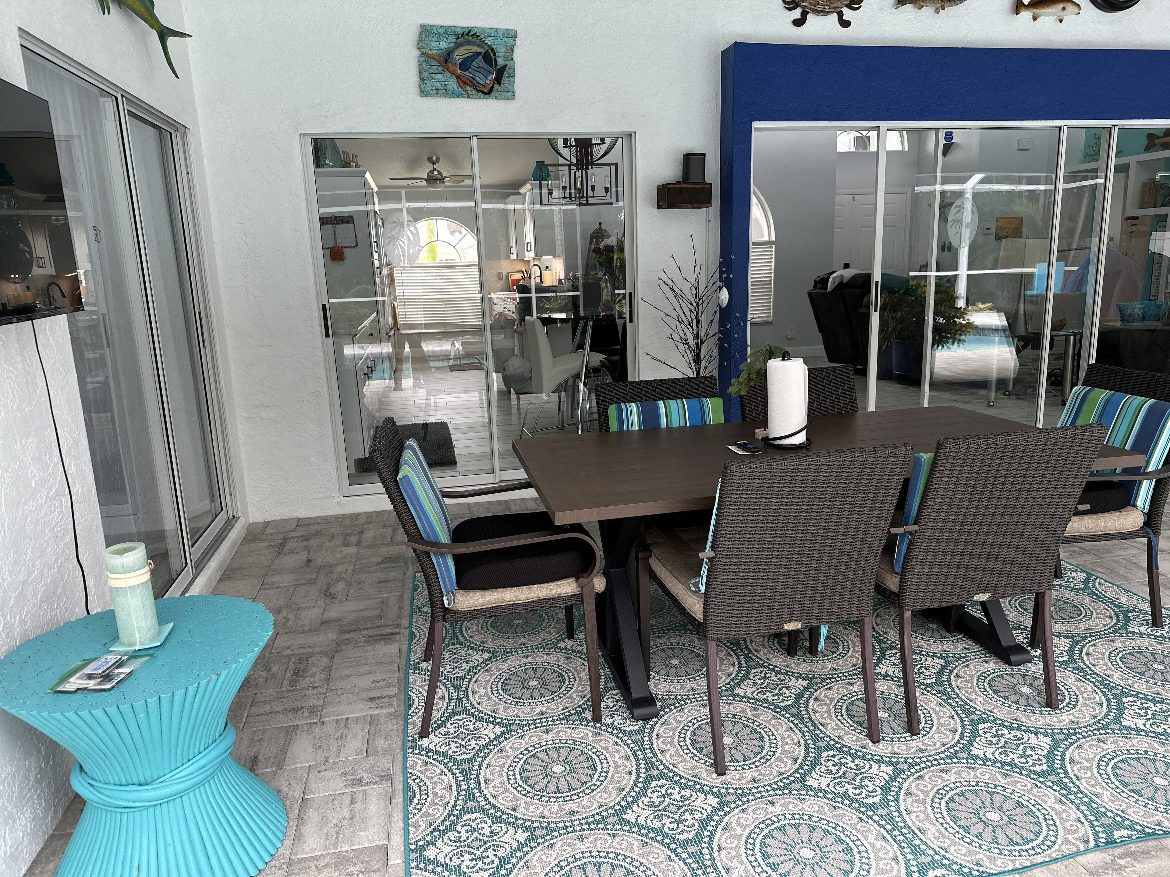 Een eethoek met een glazen deur naar een terras, rieten stoelen, een kamerbreed tapijt en een blauwe accentstoel.