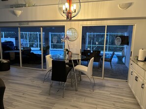 Ein moderner Essbereich mit einem Glastisch, schwarz-weißen Stühlen und einem großen Fenster mit Blick auf einen Pool und Grünflächen.