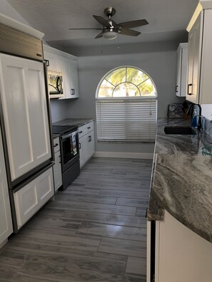A kitchen with a central island, a ceiling fan, and a window with blinds. - Cape Escape Oversized Pool Home in coveted Cape Harbor area of Cape Coral (Cape Coral)