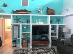Ein Wohnzimmer mit Fernseher, Regalen mit Dekoration und einem Sofa.