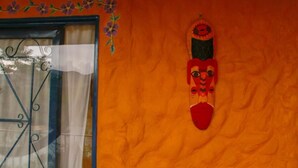 A room with a window featuring a decorative metal grill, a wall with a textured orange surface, and a wall-mounted decorative item. - Violet - with terrace, hammock (Guatapé)