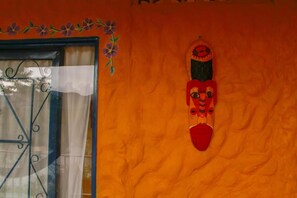A room with a window featuring a decorative metal grill, a wall with a textured orange surface, and a wall-mounted decorative item. - Violet - with terrace, hammock (Guatapé)