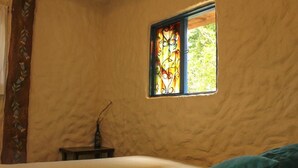 A room with a bed, a small table, and a window with a stained glass design. - Violet - with terrace, hammock (Guatapé)