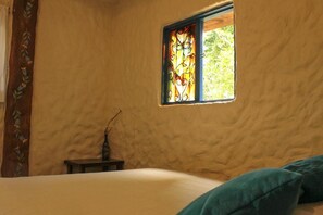 A room with a bed, a small table, and a window with a stained glass design. - Violet - with terrace, hammock (Guatapé)