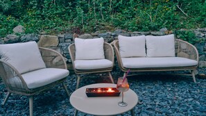A seating area with wicker chairs and a table, a lit candle, and a glass with a straw. - 3 Peaks House Modern Coastal Retreat (Penmaenmawr)