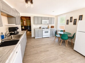 Une cuisine compacte équipée d’un évier, d’une cuisinière et d’un four à micro-ondes. Un coin repas avec une table et des chaises est également disponible.