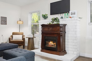 A living room with a fireplace, a sofa, a chair, a small table, and a TV mounted on the wall. - Kernville Center/Walk/2 Hot Tubs/2 Units/Mini Golf (Kernville)