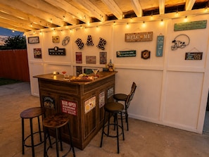 An outdoor bar area with wooden stools, a bar counter, and various signs including 'PLAY ROOM' and 'WELCOME'. - Kernville Center/Walk/2 Hot Tubs/2 Units/Mini Golf (Kernville)