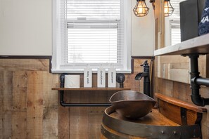 Une salle de bain avec un meuble-lavabo en bois, un lavabo blanc et une fenêtre avec des stores.