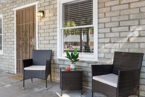 Un bâtiment avec une façade en briques, une porte en bois et deux fauteuils en osier dotés de coussins.