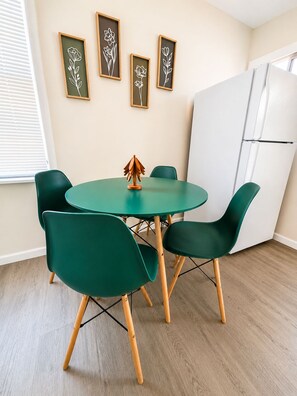A small dining area with a round table and four chairs, a white refrigerator, and framed floral artwork on the wall. - Kernville Center/Walk/2 Hot Tubs/2 Units/Mini Golf (Kernville)