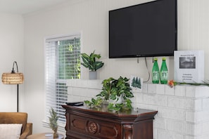 A living room with a flat-screen TV mounted on the wall, a wooden cabinet, a potted plant, and a sign on the wall. - Kernville Center/Walk/2 Hot Tubs/2 Units/Mini Golf (Kernville)