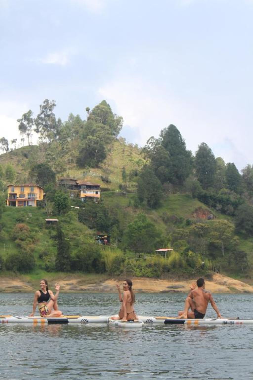 Três pessoas em uma embarcação, com paisagem montanhosa e edifícios ao fundo.