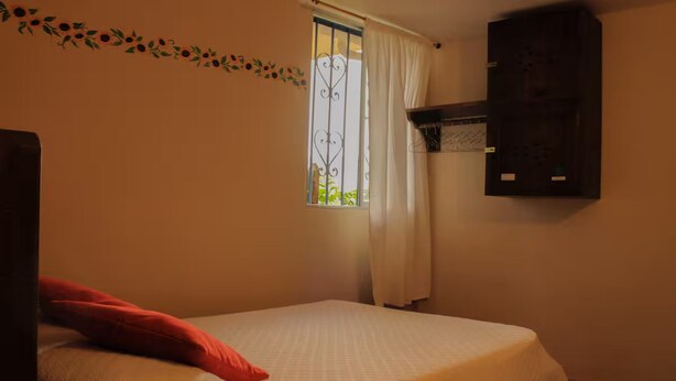 A room with a bed, a window with curtains, a wall-mounted shelf, and a decorative vine. - Girasol - Garden View (Guatapé)