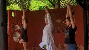 Three individuals practicing yoga in an outdoor setting with a red wall and natural surroundings. - Girasol - Garden View (Guatapé)