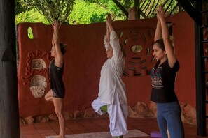 Trois personnes pratiquent le yoga en plein air, devant un mur rouge et dans un environnement naturel.