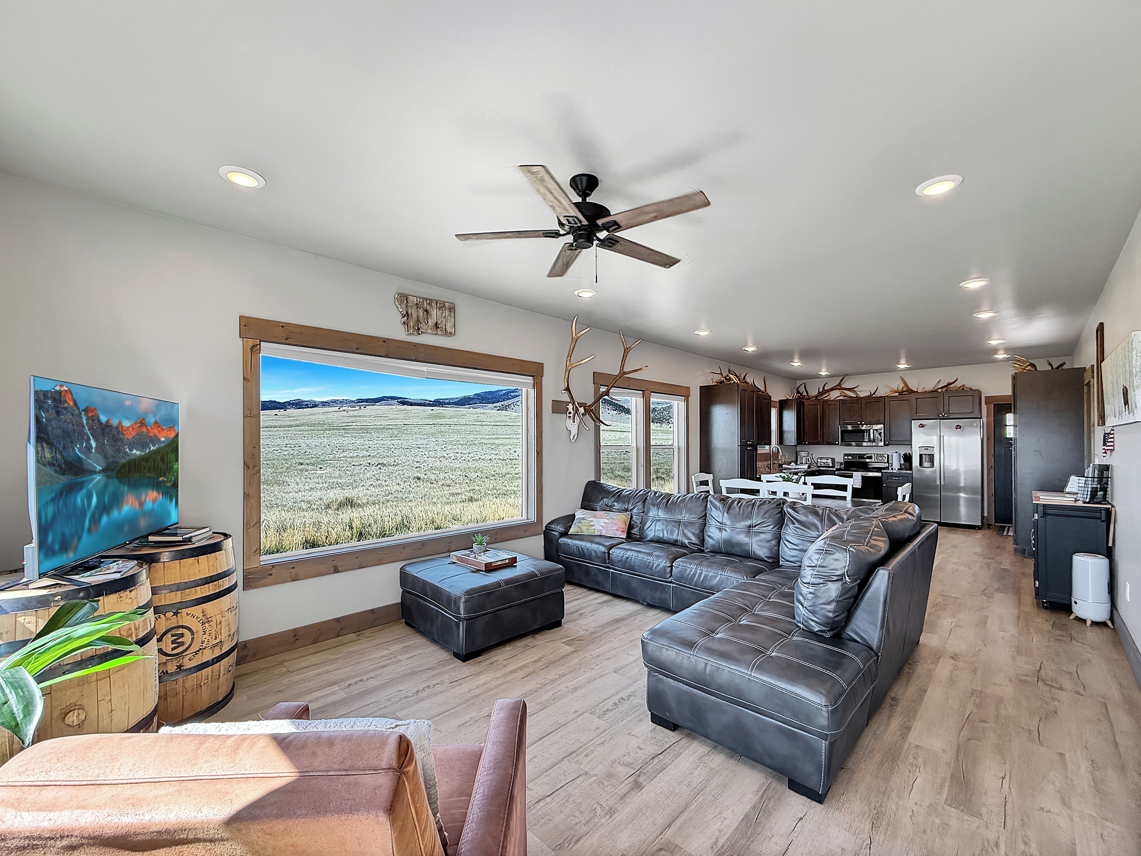 A modern living room with a sectional sofa, a ceiling fan, and a large window overlooking a field.
