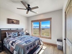 Un dormitorio con una cama grande, ventilador de techo, ventana con vista a la montaña y decoración de pared con motivos de oso.