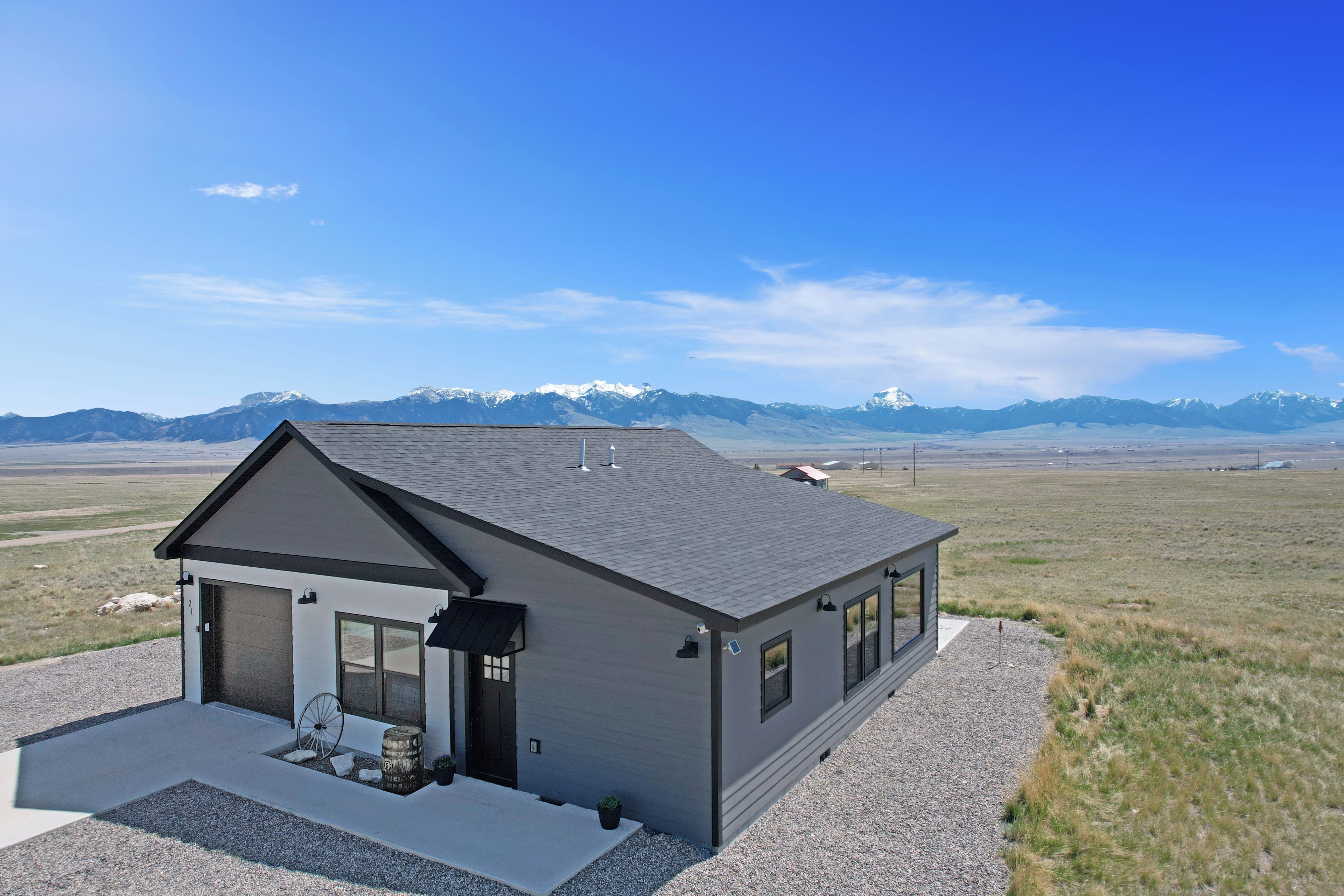A modern two-story house with a sloped roof, large windows, and a view of snow-capped mountains in the background.