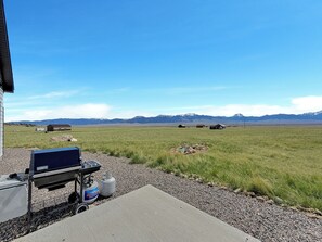 Un patio con una parrilla y tanques de propano, con vista a un campo cubierto de césped y montañas lejanas.