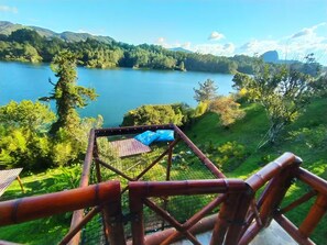 A view from a wooden deck overlooking a lake with a forested landscape in the background. - Papiro Guadua Deluxe - Cabin (Guatapé)