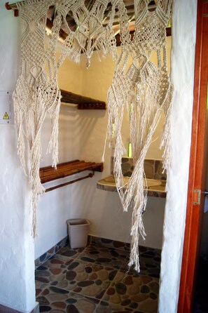 A macrame hanging chair with a stone-tiled floor and a wooden shelf. - Papiro Guadua Deluxe - Cabin (Guatapé)