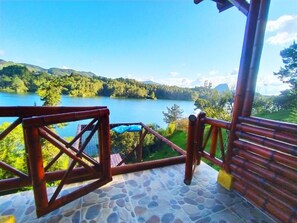 Una terrassa de lloses de pedra amb barana de fusta amb vista a un llac i turons boscosos.